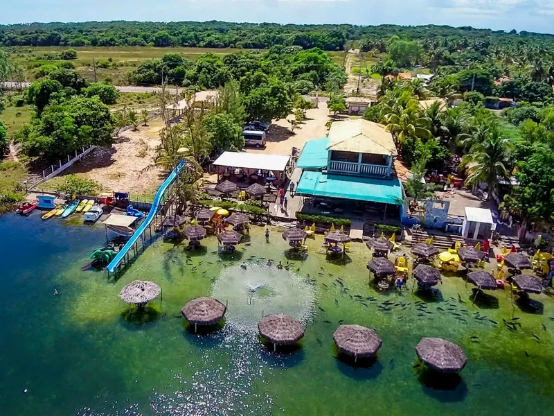 Vista aérea do espaço da lagoa, com os quiosques de palha dentro da água, o tobogã, o restaurante e a mata em volta