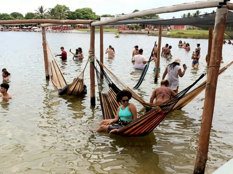 Pessoas deitadas em redes armadas dentro da água rasa da lagoa